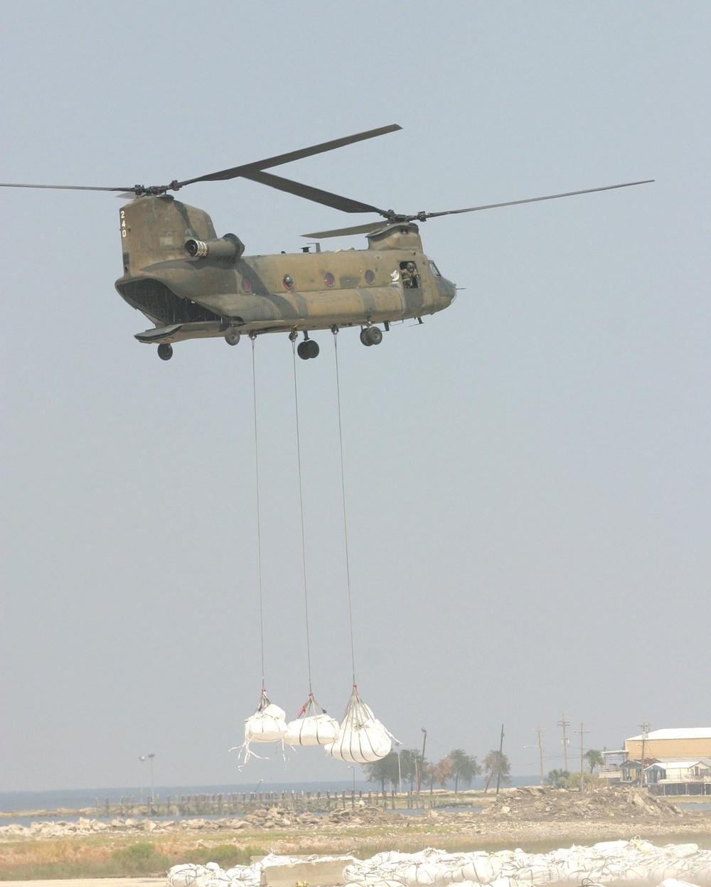 A CH-47 Chinook Helicopter Picks Up Three Large Sandbags From a Staging Are