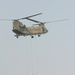 A CH-47 Chinook Helicopter Picks Up Three Large Sandbags From a Staging Are