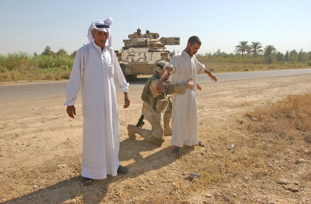 Spc. Jeromy Taylor searches Iraqi men at a traffic check point