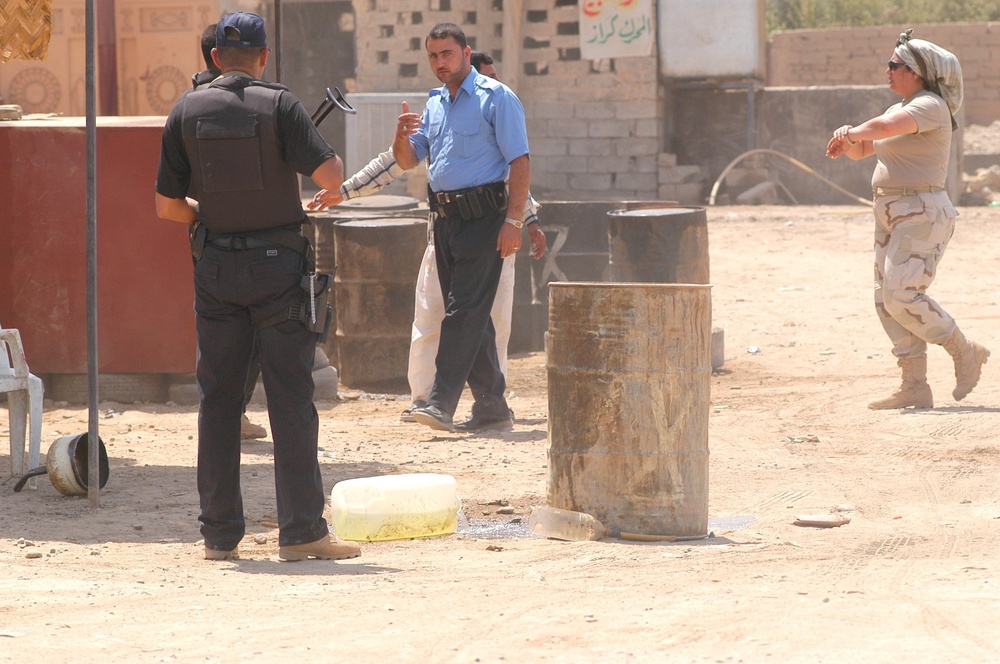 Iraqi policemen pour out plastic containers of fuel