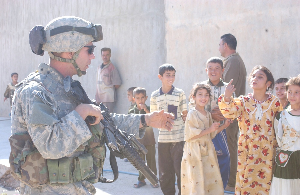 Pfc. John C. Reed motions to a group of children
