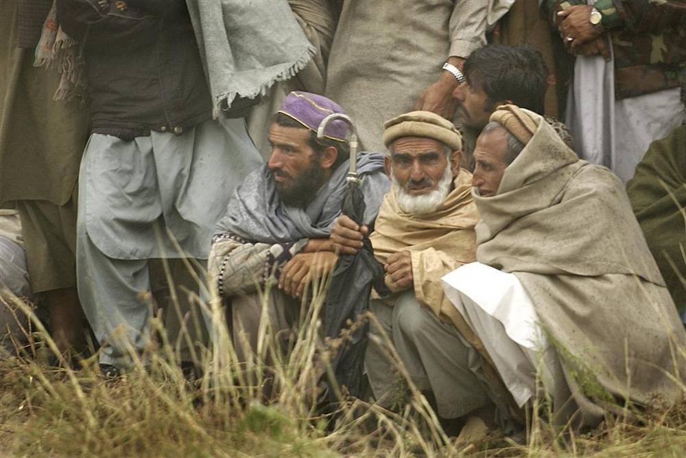 Village residents wait as Pakistani soldiers unload disaster relief supplie