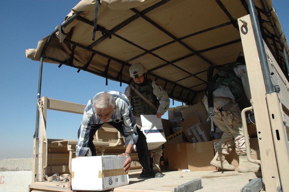 Two Soldiers help a local Iraqi man unload school supplies