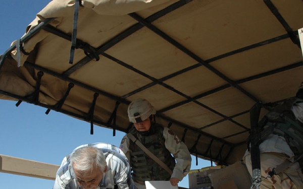 Two Soldiers help a local Iraqi man unload school supplies