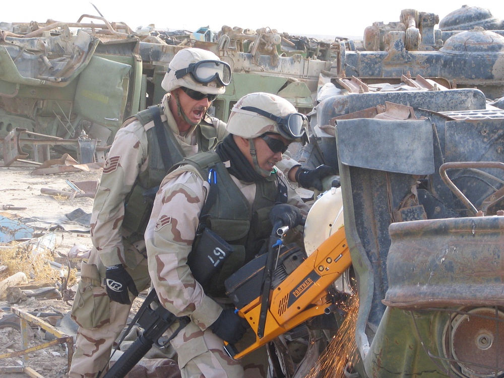 A1C Cruz and Tech. Sgt. Ralls use a K-12 to saw on the hinges of a vehicle