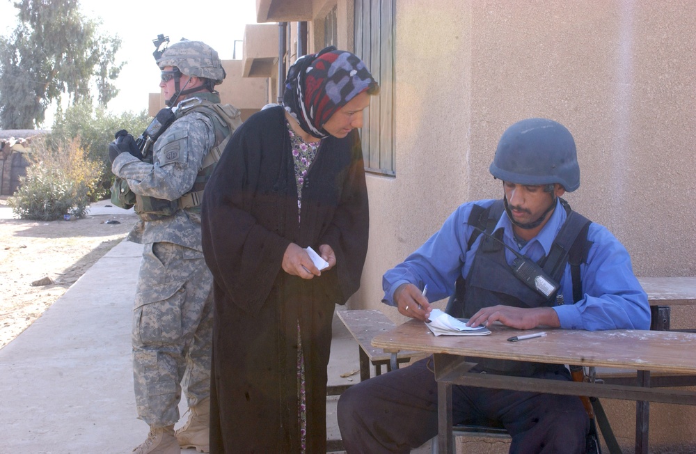 An Iraqi police officer marks a woman's ration card