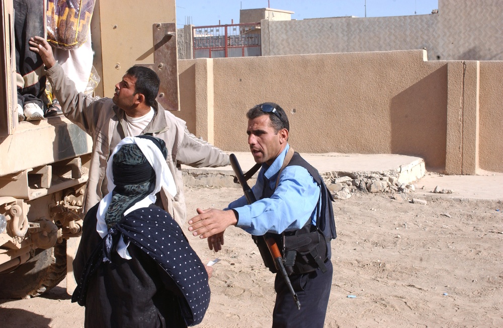 An Iraqi police officer directs a woman to a truck