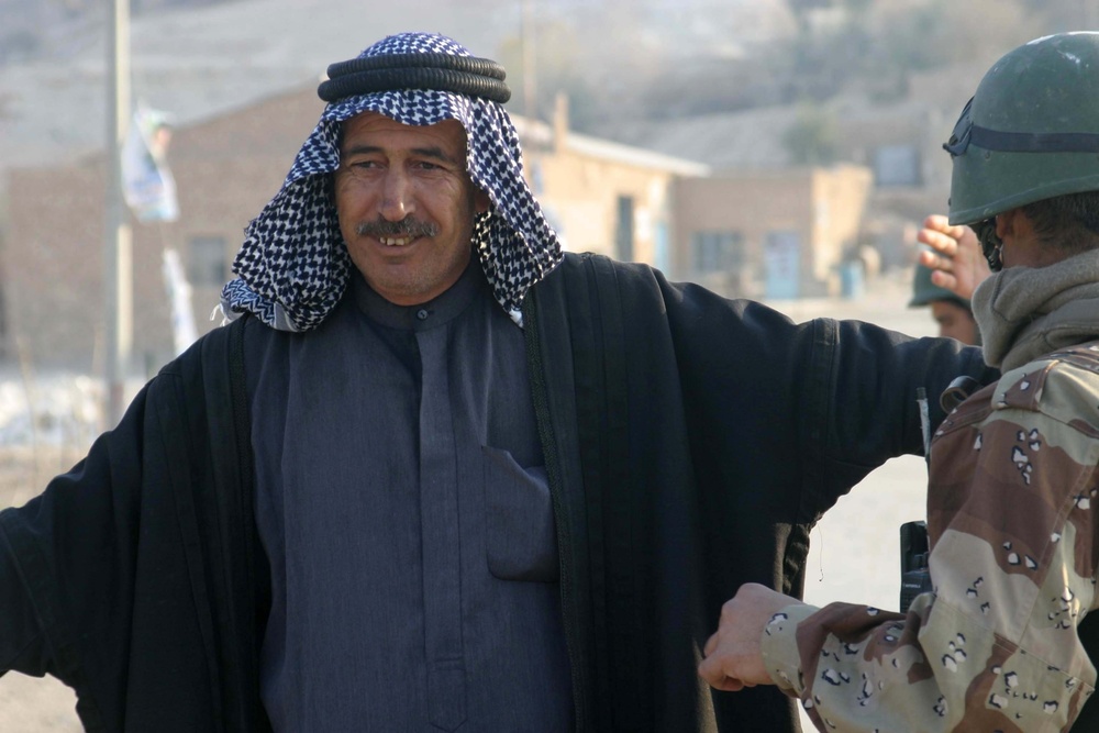 An Iraqi man holds his hands out as he is searched