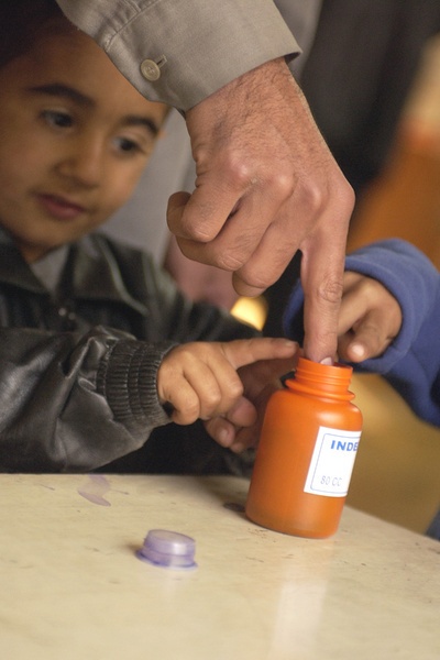 An Iraqi Boy Looks on as His Father Dips His Finger in the Purple Ink