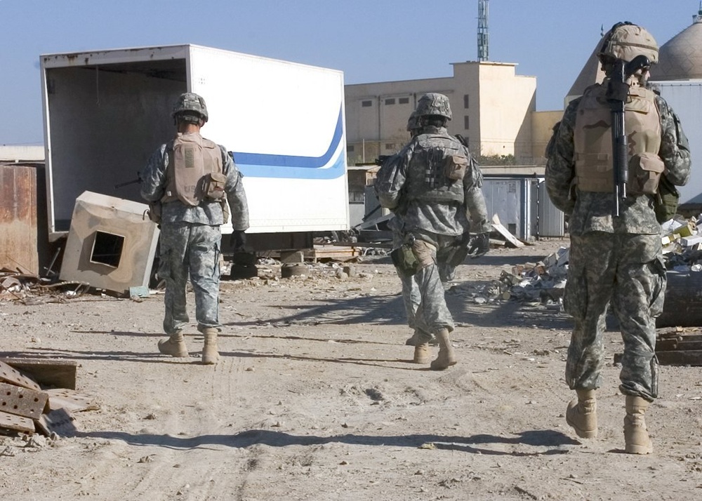 Soldiers search through twisted metal and rubble at a truck yard