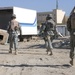 Soldiers search through twisted metal and rubble at a truck yard