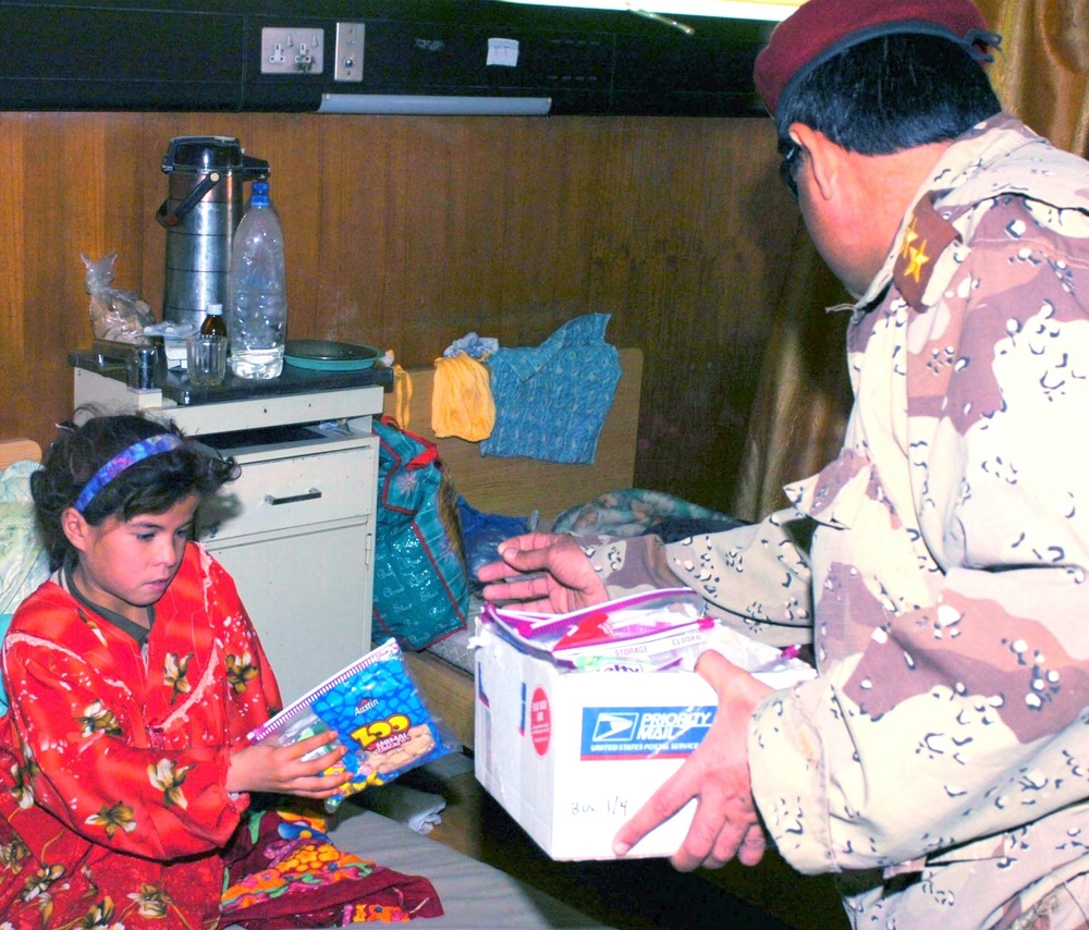 An Iraqi Army officer hands a sick Iraqi girl a bag of snacks