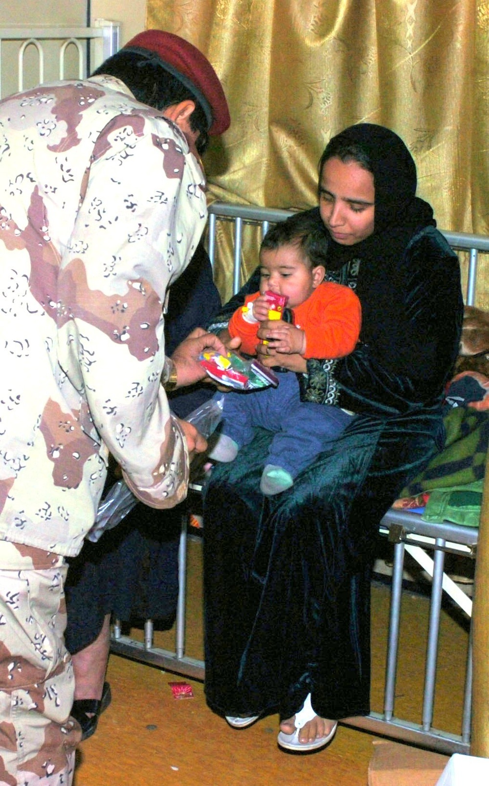 An Iraqi Army officer hands the mother of a sick Iraqi girl a bag of snacks