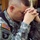 A U.S. Army soldier wearing Army Combat Uniform (ACU) is shown in a bowed-head, hands-clasped prayer position. The soldier's patches identify affiliation with the 101st Airborne Division and bears a name tape partially reading 'JONES'. The image conveys a moment of personal reflection or religious observance.