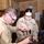 Two U.S. Army soldiers in Desert Combat Uniform (DCU) are working at a workbench in what appears to be a field armory or maintenance shop. Both are wearing safety glasses and are engaged in what appears to be weapons maintenance or repair work using hand tools. The female soldier's name tape reads 'MELSON' and she is holding a ball-peen hammer.