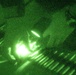 This image was captured through night vision optics, producing the characteristic green monochromatic appearance. A bright central light source dominates the frame, surrounded by blurred and grainy elements suggesting motion or low-light conditions. The image quality is heavily degraded due to the night vision amplification and apparent camera movement.
