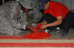 Spc. Benita Barnes, a cook with the 368th Cargo Transportation Company out of Ft. Story, Va., and a civilian contractor add red food coloring to white rice. The rice was then used to create a large American flag and was spread across the floor of DFAC 1 a