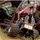 A small robotic vehicle with large off-road wheels is positioned at the open door of a damaged dark red Toyota Camry. The car's windshield is shattered in a spider-web pattern, and the vehicle appears to have sustained significant damage. The robot appears to be a remote-controlled reconnaissance or bomb disposal unit being used to inspect the vehicle interior.