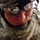 A close-up photograph of a U.S. Army soldier in full combat gear, wearing Army Combat Uniform (ACU) in Universal Camouflage Pattern. The soldier's name tape reads 'GEULHAR' (partially visible) and displays a Sergeant rank insignia (chevron with rocker). The soldier is wearing protective ballistic eyewear and a combat helmet, with face showing signs of heat and exertion.