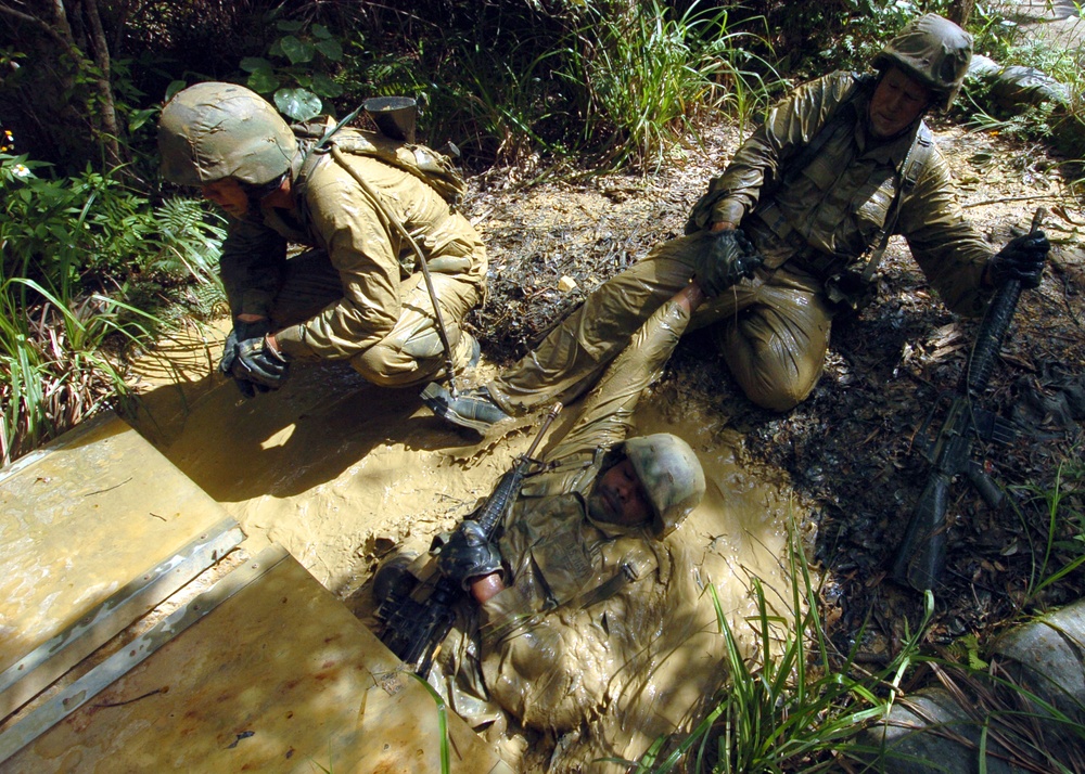 Seabees exit mud-filled trench during jungle training evolution