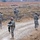 Sappers clear dangerous route essential to Operation Raider Harvest The image shows a group of approximately five to six military personnel in ACU (Army Combat Uniform) digital camouflage conducting a patrol along a dirt road in an arid, open terrain. The soldiers are spread out in a tactical formation, carrying weapons and wearing full combat gear including helmets and body armor. The landscape appears dry and sparse, consistent with a Middle Eastern or Central Asian operational environment.