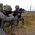 Sappers clear dangerous route essential to Operation Raider Harvest Two U.S. Army soldiers in Universal Camouflage Pattern (UCP) ACU uniforms are taking up defensive firing positions in what appears to be a rural Middle Eastern environment. Both soldiers are aiming M4 carbine rifles equipped with optics and accessories. The setting, vegetation, and architecture in the background are consistent with operations in Iraq or Afghanistan.