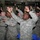 A large group of U.S. Army soldiers in ACU (Army Combat Uniform) digital camouflage are gathered in what appears to be a recreational facility or gymnasium, with their hands raised in the air in a celebratory or participatory gesture. The soldiers appear to be engaged in a group activity, possibly a morale event, performance, or organized entertainment. The atmosphere appears upbeat and energetic, with many soldiers smiling.