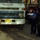 Iraqi Security Force take lead during Ashura movement in Kadhimiyah A street scene showing two men reviewing documents beside a weathered Nissan Diesel truck with visible rust and a yellow license plate. A police vehicle numbered '790' is parked nearby, suggesting this may be a traffic stop or vehicle inspection. The setting appears to be an urban street in the Middle East, likely Iraq, based on Arabic signage visible in the background.