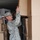 A U.S. Army soldier in Army Combat Uniform (ACU) digital camouflage pattern is loading or unloading large cardboard boxes inside what appears to be a shipping container or cargo truck. The soldier is smiling while lifting a large box overhead, surrounded by stacked cardboard boxes on multiple sides. The setting suggests a military logistics or supply operation.