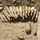 The image shows a collection of recovered or seized munitions laid out on sandy/dirt ground. The items appear heavily corroded and soil-encrusted, suggesting they were excavated or recovered from burial. This appears consistent with a cache discovery or ordnance disposal documentation photograph.