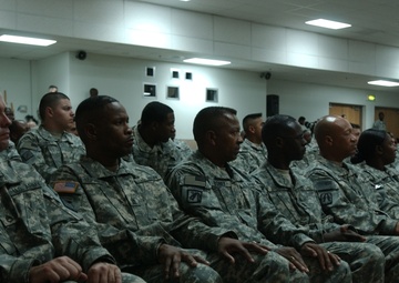 A group of U.S. Army soldiers in ACU (Army Combat Uniform) digital camouflage are seated in rows inside what appears to be a briefing room or auditorium. The soldiers are attentively seated, suggesting they are attending a formal military briefing, ceremony, or training event. A sign visible in the lower left reads 'SAMC/SMC MEMBERS', indicating this may be a Sergeant Major course or senior NCO event.