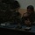 A military officer in camouflage uniform sits at a desk in what appears to be a command post or field office. He is wearing shoulder patches and has a radio/walkie-talkie visible, suggesting a command role. The room contains stacked military equipment cases and ammunition boxes in the background.