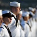 A formation of U.S. Navy sailors dressed in white dress uniforms are standing at attention in a disciplined line. The focal point is a female sailor in the foreground wearing a combination cover (white cap with black brim) and a black neckerchief. A name tape reading 'USS Abraham Lincoln' is visible on her uniform, suggesting this is a naval ceremony or formal muster.