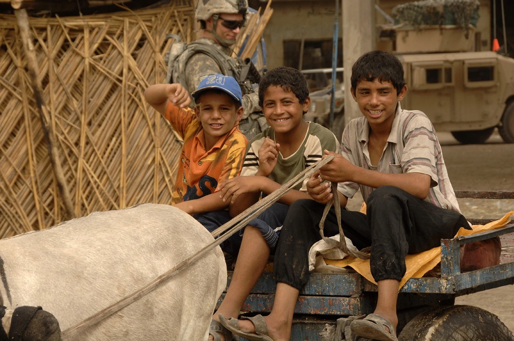 Iraqi Children Ride Past Guarding Soldiers