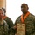 Two U.S. Army soldiers in ACU (Army Combat Uniform) camouflage are posing together while holding a framed certificate or award. Both soldiers are wearing orange lanyards/medals around their necks, suggesting a formal recognition ceremony. A third soldier is partially visible in the background.