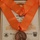 The image shows a U.S. Army Signal Corps Association 'Order of Mercury' medal suspended on an orange ribbon, displayed over a framed certificate. The bronze medal features a figure of Mercury standing on a globe, with the inscription 'U.S. Army Signal Corps Association' and 'Order of Mercury'. The certificate is signed by BG Albert J. Myer, First Chief Signal Officer - 1860, United States Army, and a President identified as LTG USA Ret.