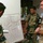 Three military personnel in camouflage uniforms are gathered around a whiteboard displaying a hand-drawn tactical map or diagram. One soldier is pointing at or presenting the map while the others observe. The setting appears to be an indoor briefing room, suggesting a military planning or coordination session.