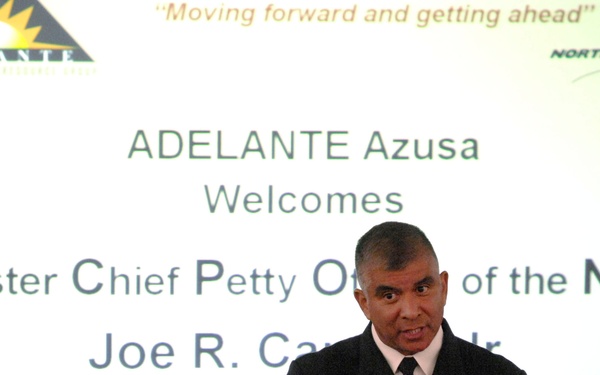 A U.S. Navy Master Chief Petty Officer is delivering a presentation or speech at an ADELANTE Azusa event, sponsored by Northrop Grumman. The projected screen behind him identifies him as 'Master Chief Petty Officer of the Navy Joe R. Ca[r]..Jr.' The officer is in full dress uniform with multiple ribbons and insignia, gesturing while speaking.