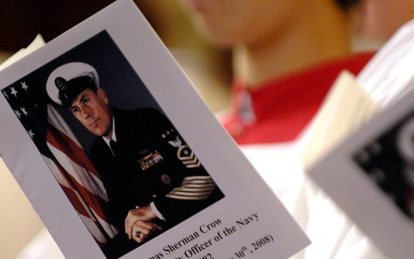 A funeral or memorial service program is being held by an attendee wearing a red and white garment. The program features a formal military portrait of Thomas Sherman Crow, a Master Chief Petty Officer of the Navy, along with his birth and death dates. Multiple attendees appear to be holding identical programs at what is clearly a memorial service.