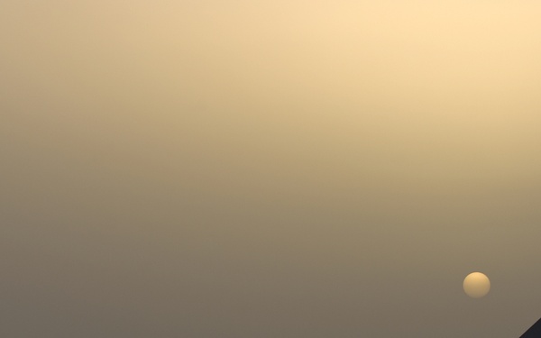 An F-16 Fighting Falcon jet fighter is parked on a tarmac during sunset or sunrise, with a hazy, dust-filtered sky casting an orange glow. The aircraft bears markings indicating it belongs to the Minnesota Air National Guard, based in Duluth. The tail number '242' and the word 'MINNESOTA' are visible on the fuselage.