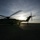 Activities at Al Asad Air Base A large military helicopter is photographed in silhouette on a tarmac or airfield at sunset or sunrise. The rotor blades are in motion, visible as motion-blurred arcs. A single human figure stands in silhouette near the rear of the aircraft, backlit by the sun.