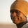 Activities at Al Asad Air Base A U.S. Marine is photographed in a close-up portrait against a desert background during golden hour lighting. The subject is smiling and wearing MARPAT desert camouflage uniform with a tan fleece beanie cap. A rank insignia patch is visible on the collar, and dog tags can be seen around the neck.