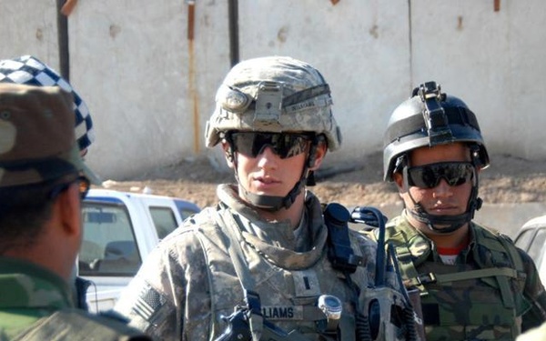 The image shows a group of military personnel in a outdoor setting, appearing to be in a briefing or coordination meeting. A U.S. Army soldier wearing ACU (Army Combat Uniform) with the name tape 'WILLIAMS' is prominently visible in the center, interacting with what appear to be local or allied forces. The setting suggests a forward operating base or checkpoint environment in a Middle Eastern location.