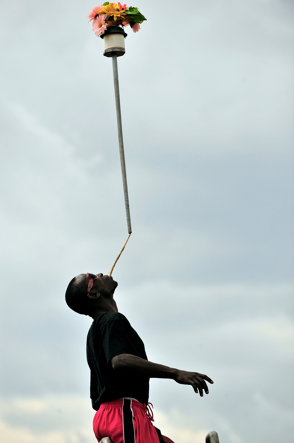 A Uganda Peoples Defense Force Soldier Stands on a Ladder, Balancing a Potted Plant on a Pole in His Mouth, During a Graduation Ceremony at the UPDF Non-Commissioned Officers Academy in Jinja.