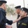 The image shows a group of uniformed personnel, likely a police or security force, engaged in what appears to be an inspection or formation activity. A senior officer is examining or adjusting the collar/uniform of a subordinate officer. The uniforms display Arabic script patches and English text reading 'Security Forces'.