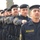A formation of uniformed personnel from the 'Oil Protection Force' standing at attention in a disciplined line. The personnel wear dark navy/black uniforms with yellow Arabic and English text patches, and black berets with insignia badges. This appears to be a formal parade or inspection ceremony.