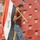 A young man carries a large Iraqi flag on a gold-tipped pole while walking through the stands of a stadium with predominantly empty red seats. The flag displays the distinctive red, white, and black horizontal stripes with green Arabic script in the center. The setting appears to be before or after a sporting event.