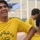 The image shows several young men wearing matching yellow jerseys with Arabic text and the brand name 'alsied'. The foreground subject is laughing broadly, suggesting a lighthearted, candid moment likely during a sports training session or team gathering. The setting appears to be a stadium, visible from the seating stands in the blurred background.