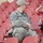 A U.S. Army soldier in ACU (Army Combat Uniform) is seated in red stadium bleachers while a young boy in a red shirt stands nearby appearing to salute or shade his eyes. The soldier's name tape reads 'FOSTER' or similar. The setting appears to be a sports stadium with many empty red seats visible in the background.