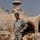 A U.S. Army soldier in ACU (Army Combat Uniform) stands among unusual dome-shaped, organic-form concrete or adobe structures covered in graffiti. The structures have rounded, mushroom-like architectural forms with tunnel/arch openings, and palm trees are visible in the background suggesting a Middle Eastern or arid environment. Multiple graffiti inscriptions in Spanish ('TE AMO', 'VERO') and English are visible on the structures.